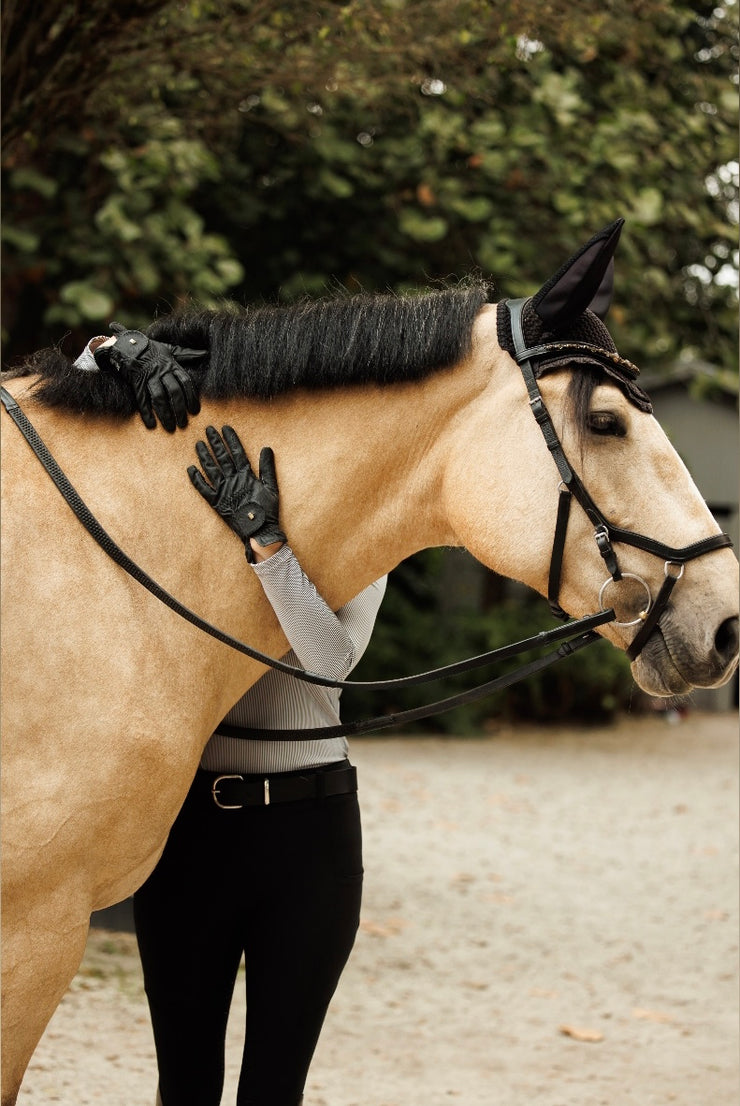 Woman standing behind her horse hugging his neck. You can see the sleeves of her Charlie blouse and her black gloves and black breeches