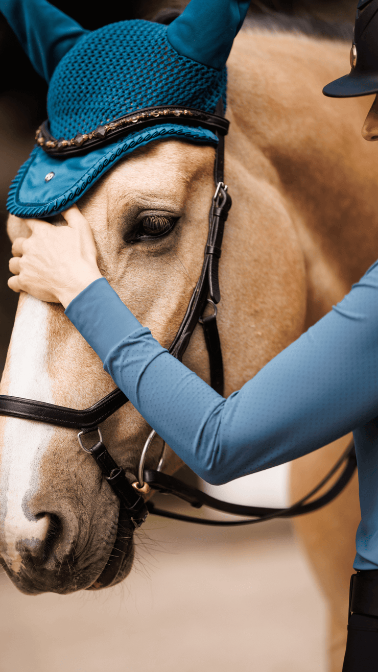 Woman wearing the Marina equestrian riding shirt. She is showing off the perforated arms and cuffs of the long sleeves and the wave like pattern of the mock neck.