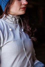 Woman wearing heathered oatmeal colored GG Technical Shirt with corded earbuds threaded through the keepers on the neck. She is wearing a blue beanie and has her hair in a pony tail to the left side of her face. You only see her from the nose down. 